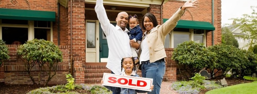 A family celebreates in front of their home with a sold sign